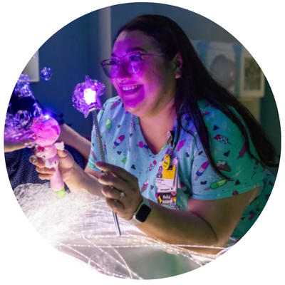 Image of UIHC Medical assistant Lizeth DeLeon, young woman with long brown hair wearing scrubs, uses sensory toy distractions to put patients at ease in the comfort room at the Center for Disabilities and Development.